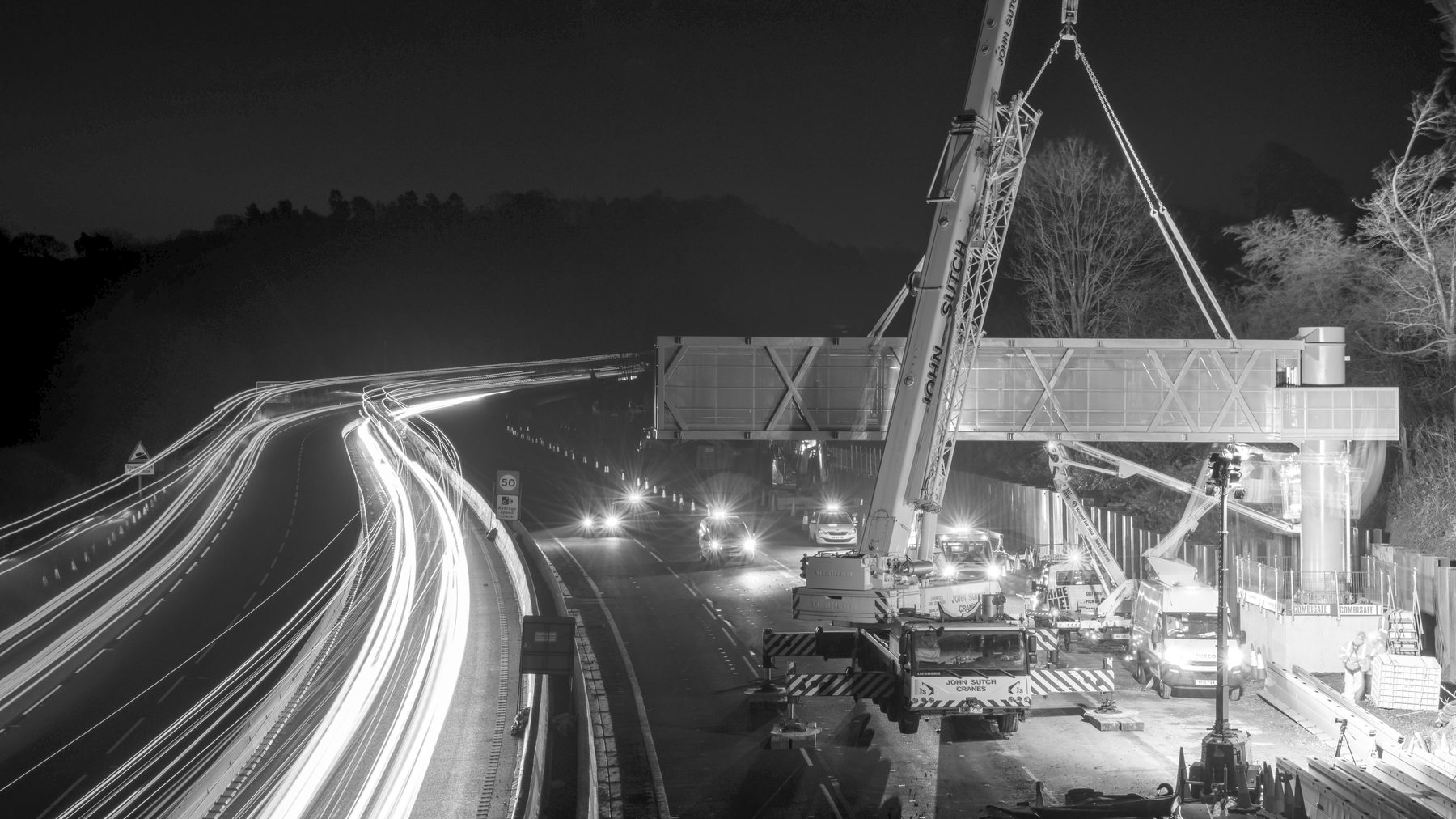 A gantry being lifted into place over a motorway at night